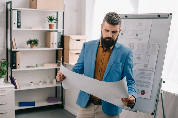 Beau architecte debout et regardant le papier dans le bureau moderne — Photo de stock