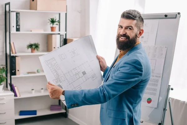 Arquitecto guapo de pie en la oficina moderna con plano - foto de stock