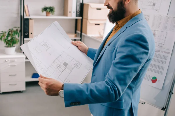 Обрезанный вид взрослого мужчины-архитектора в синей формальной одежде, держащего чертеж, использующего флип-чарт и работающего над проектом в офисе — стоковое фото