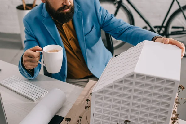 Abgeschnittene Ansicht eines erwachsenen männlichen Architekten in formaler Kleidung, der eine Tasse Kaffee hält und im Büro an einem Projekt arbeitet — Stockfoto