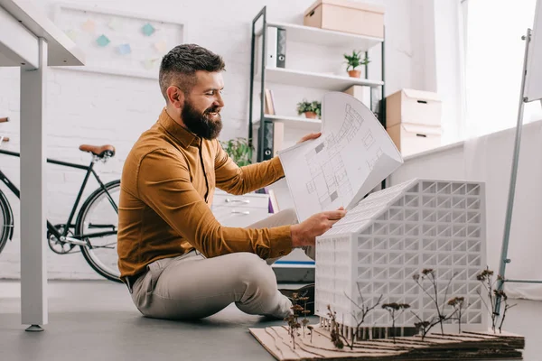 Sourire barbu adulte architecte masculin travaillant sur un projet de construction avec modèle de maison dans le bureau — Photo de stock