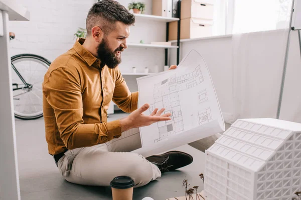 Angry bearded adult male architect holding blueprint and working on project in office — Stock Photo