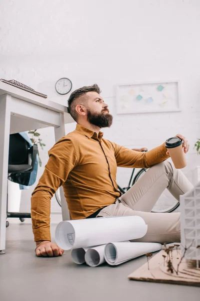 Serious bearded adult male architect holding coffee to go and working on construction project with blueprints in office — Stock Photo