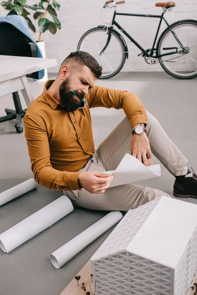 Konzentrierter erwachsener, bärtiger Architekt sitzt auf dem Boden und arbeitet im Büro an Entwürfen — Stockfoto