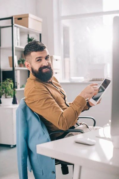 Hombre de negocios adulto sonriente sentado en el escritorio de la oficina y el uso de tabletas digitales en el lugar de trabajo - foto de stock