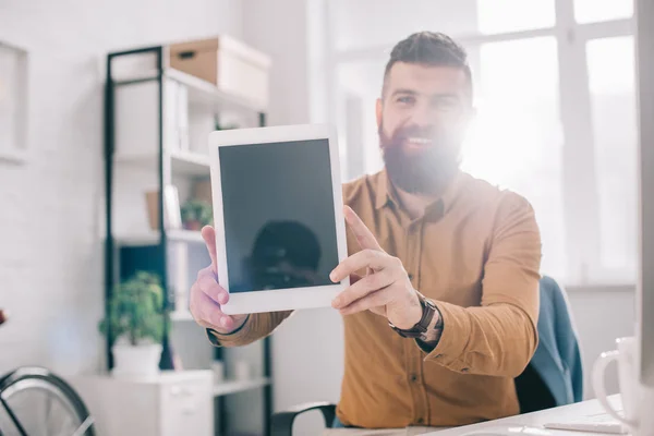 Hombre de negocios adulto sonriente que presenta tableta digital con pantalla en blanco en el lugar de trabajo con retroiluminación - foto de stock
