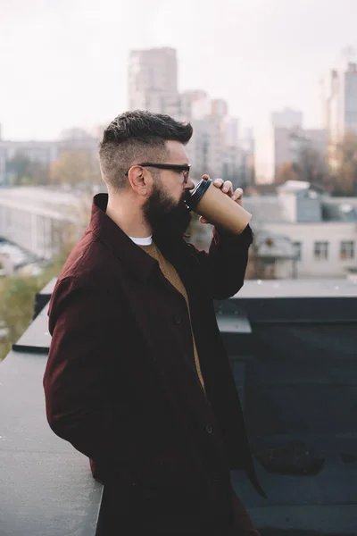 Stylish adult man in glasses holding coffee to go on rooftop — Stock Photo