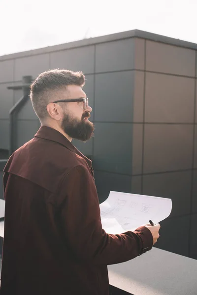 Schöner erwachsener Architekt in Brille mit Blaupause auf dem Dach — Stockfoto