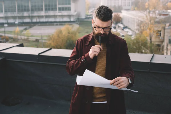 Pensive adult male architect in glasses holding blueprint and working on project on rooftop — Stock Photo