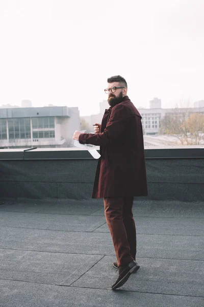 Erwachsener männlicher Architekt in Brille mit Blaupause und Blick auf die Kamera auf dem Dach — Stockfoto