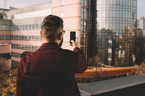 Vista trasera del hombre adulto tomando selfie en la azotea con hermosa vista - foto de stock