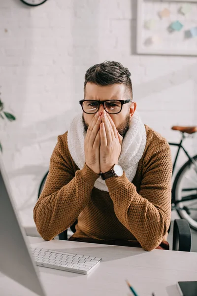 Homme d'affaires malade en écharpe tricotée assis au bureau, toussant et couvrant la bouche avec les mains — Photo de stock