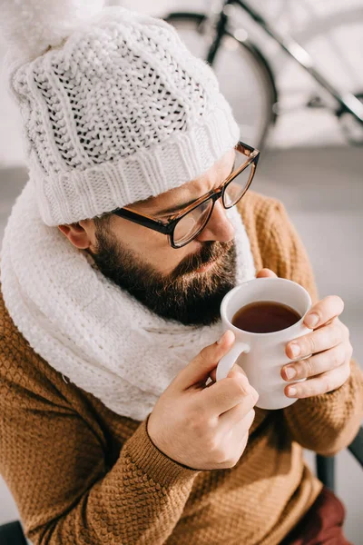 Close up of sick man in scarf and knitted hat holding cup of tea — Stock Photo