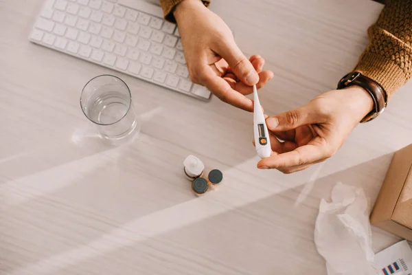 Cropped view of businessman holding medical thermometer at office desk — Stock Photo