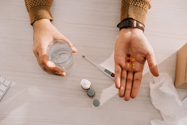 Ausgeschnittene Ansicht eines Geschäftsmannes, der Tabletten und ein Glas Wasser am Schreibtisch hält — Stockfoto