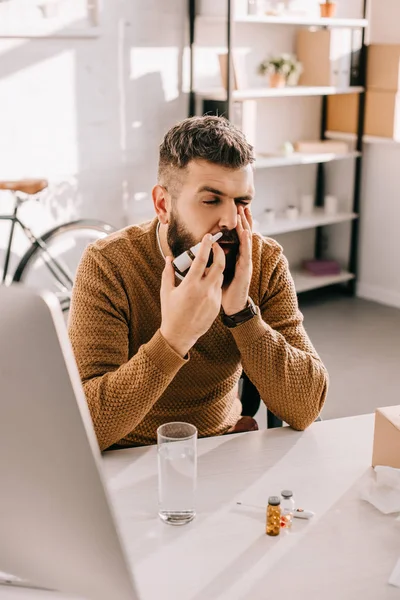 Empresário doente sentado na mesa do escritório com escorrendo usando spray nasal — Fotografia de Stock