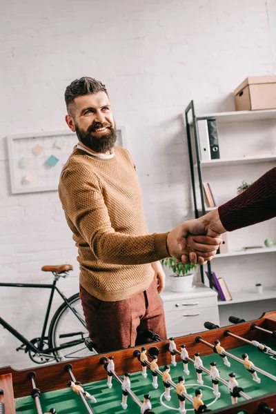 Sonriente hombre adulto estrechando la mano con amigo después de jugar fútbol de mesa juego - foto de stock