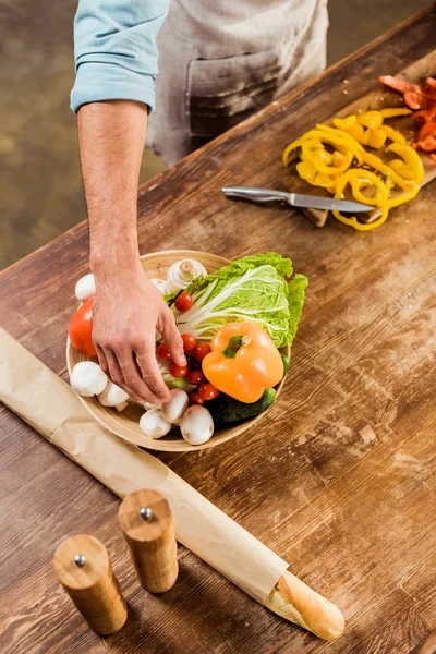 Colpo ritagliato di uomo in grembiule cottura insalata di verdure in cucina — Foto stock