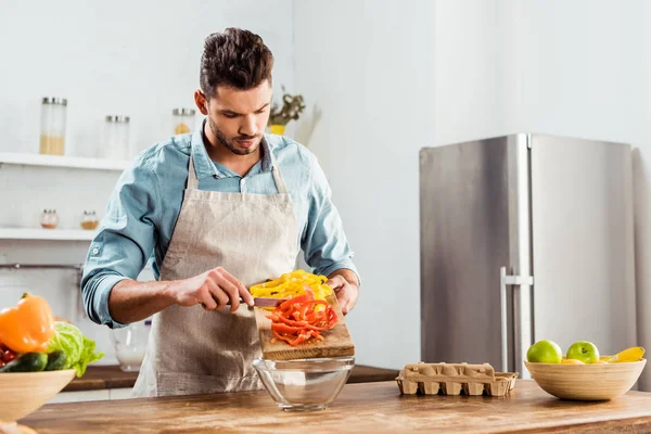 Young man in apron preparing vegetable salad in kitchen — Stock Photo