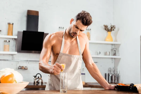 Sexy young man in apron squeezing lemon in glass — Stock Photo