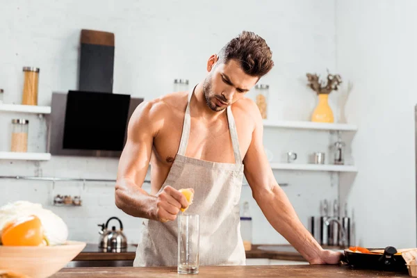 Sexy junger Mann in Schürze, der Zitrone ins Glas drückt — Stockfoto