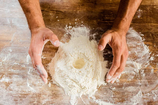 Vista parcial de las manos masculinas y harina en la mesa de la cocina - foto de stock