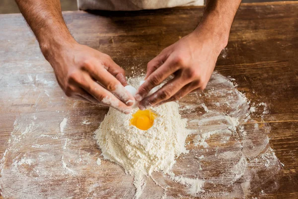 Обрезанный кадр человека, готовящего тесто с мукой и яйцом на кухонном столе — стоковое фото
