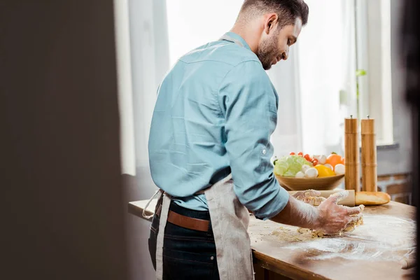 Visão traseira do jovem no avental preparando massa na cozinha — Fotografia de Stock