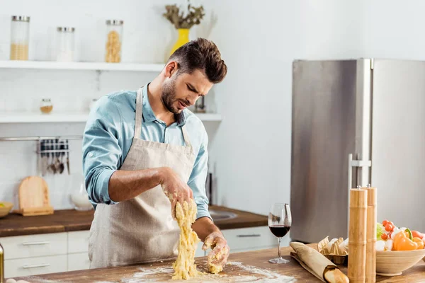 Upset young man in apron looking at spoiled dough on hands — Stock Photo
