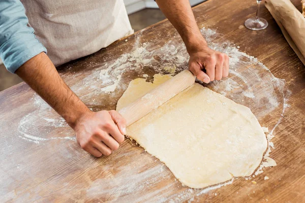 Cropped shot of young man in apron holding rolling pin and preparing dough in kitchen — Stock Photo