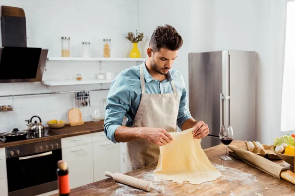 Bel giovanotto in grembiule che prepara la pasta in cucina — Foto stock