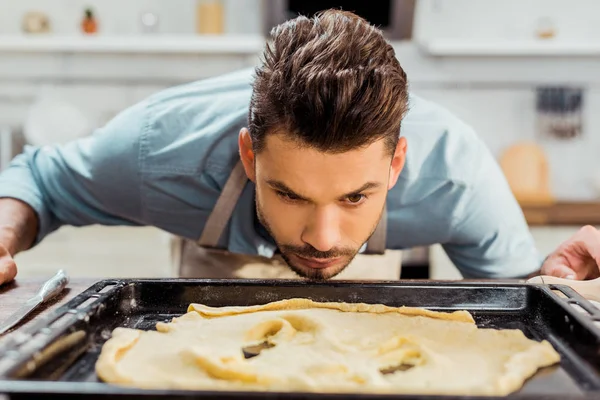 Junger Mann in Schürze betrachtet verdorbenen Teig auf Backblech — Stockfoto