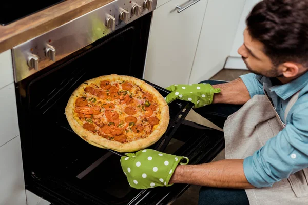 Tiro cortado de jovem tirando bandeja de cozimento com pizza do forno — Stock Photo