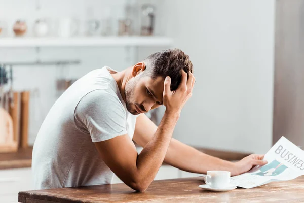 Joven molesto leyendo el periódico en la cocina por la mañana - foto de stock