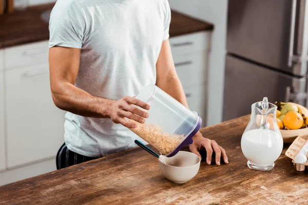 Schnappschuss von jungem Mann, der Container mit Cornflakes hält und in Küche Frühstück zubereitet — Stockfoto