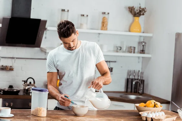 Giovane uomo versando il latte nella ciotola con fiocchi di mais al mattino — Foto stock