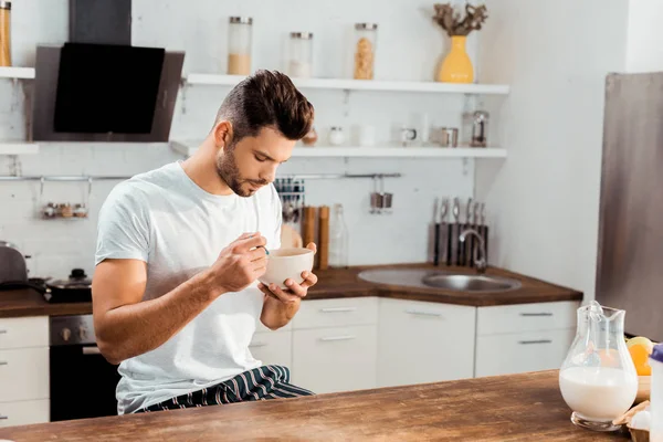 Junger Mann im Pyjama isst zu Hause Cornflakes zum Frühstück — Stockfoto