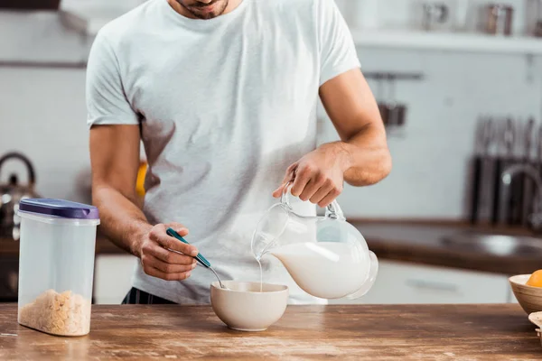 Tiro recortado de hombre vertiendo leche en un tazón con hojuelas de maíz para el desayuno - foto de stock