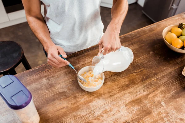 Colpo ritagliato di uomo versando latte in ciotola con fiocchi di mais — Foto stock