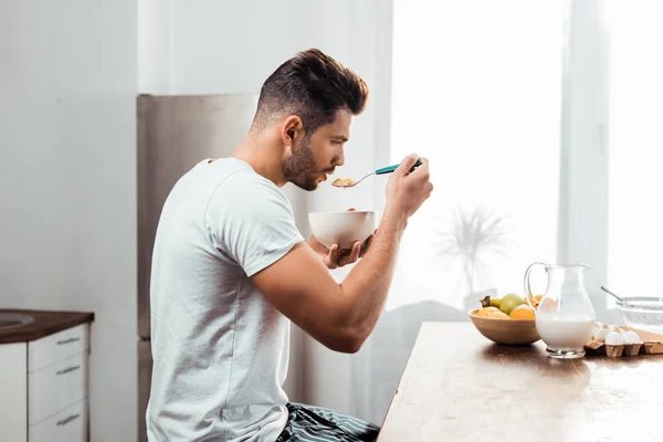 Side view of young man in pajamas eating cereals for breakfast at home — Stock Photo