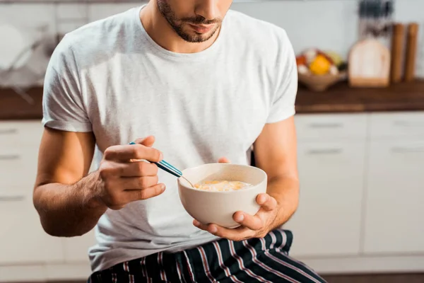 Cropped shot of young man in pajamas eating cereals for breakfast at home — Stock Photo