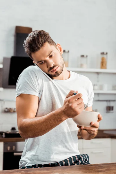 Giovane in pigiama che fa colazione e parla con lo smartphone — Foto stock