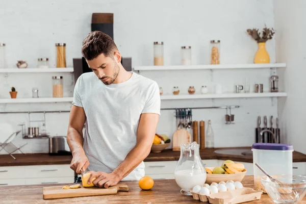 Красивый молодой человек режет лимон на кухонной доске — Stock Photo