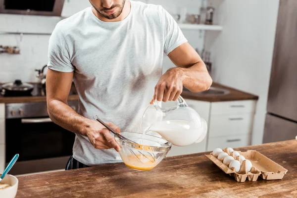 Plan recadré de jeune homme versant du lait et omelette de cuisson le matin — Photo de stock