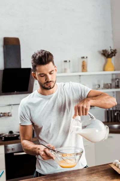 Jeune homme versant du lait et omelette de cuisine le matin — Photo de stock