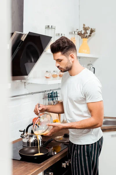 Красивый молодой человек в пижаме готовит омлет на сковородке — стоковое фото
