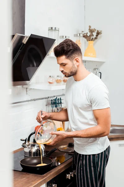 Bel giovanotto in pigiama che cucina frittata in padella — Foto stock