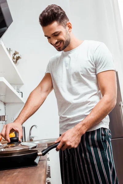 Visão de baixo ângulo do jovem sorridente em pijama omelete de cozinha na frigideira — Fotografia de Stock