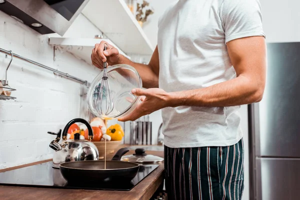 Sección media del joven en pijama tortilla de cocina en la sartén - foto de stock