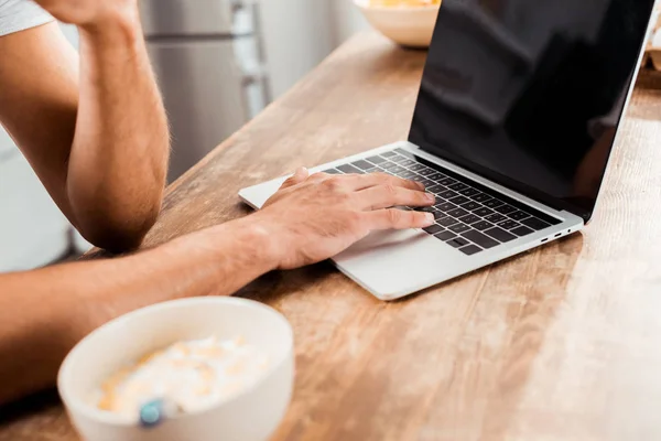 Ritagliato colpo di uomo utilizzando computer portatile con schermo bianco sul tavolo della cucina al mattino — Foto stock